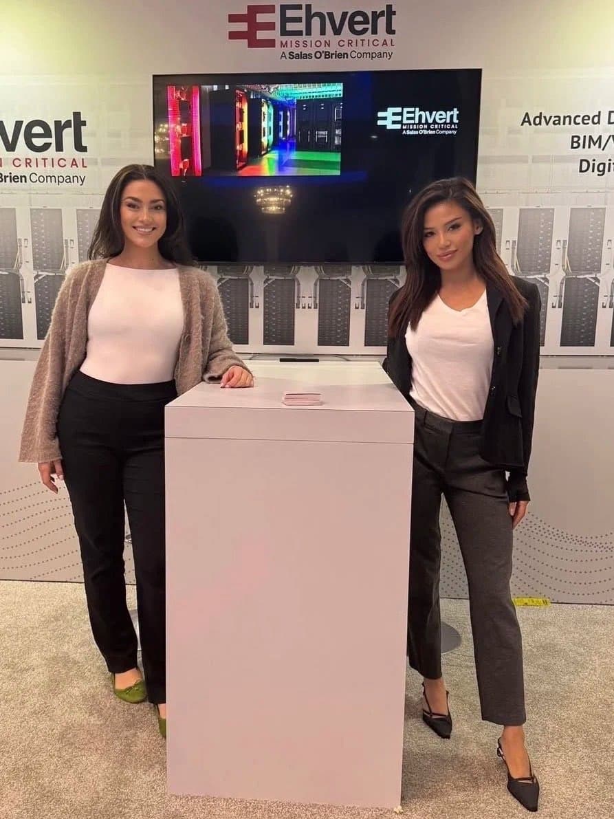 Two brand ambassadors in business attire staff the Ehvert Mission Critical booth, its screen showing a data center, at a technology trade show.