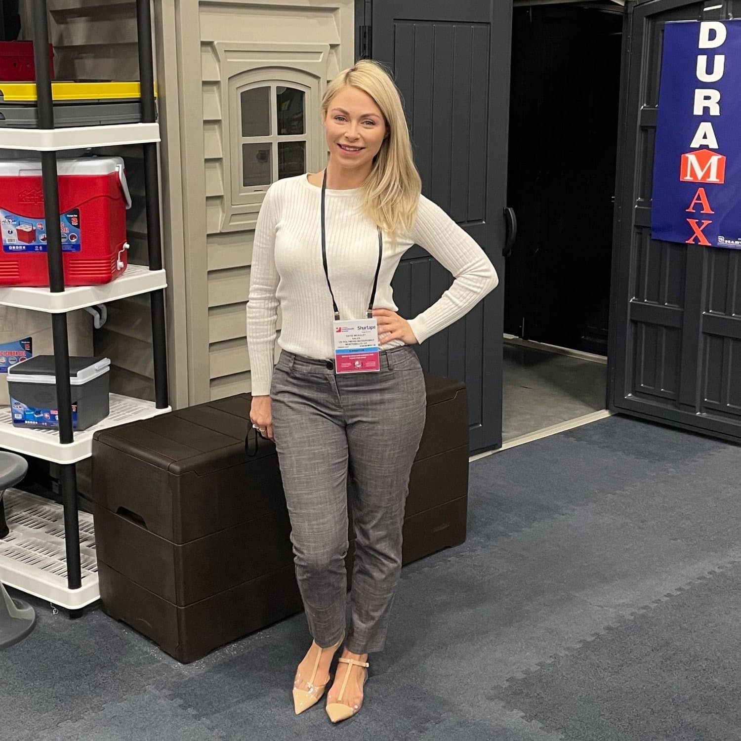 A brand ambassador wearing a Shurtape event badge stands in front of a trade show booth displaying Duramax storage sheds and coolers.